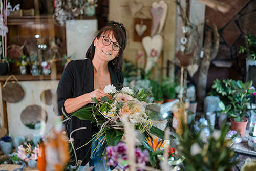 Floristin bindet Blumenstrauß und lächelt dabei in die Kamera